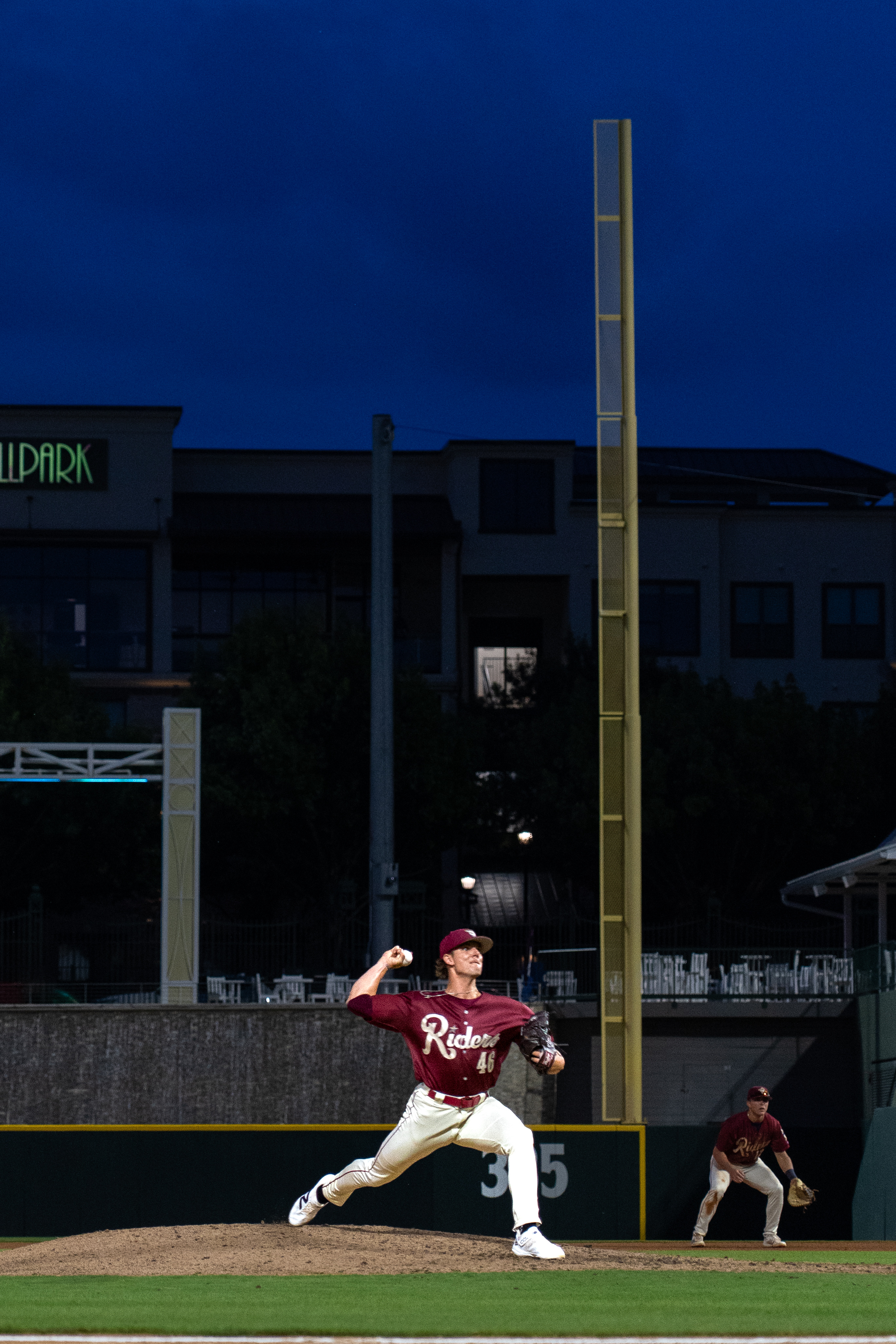 A baseball pitcher mid-delivery on the mound during a game at dusk